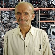 Man with a salt-and-pepper mustache and thinning hair, standing in front of an array of auto parts